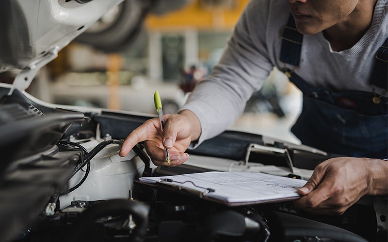 A man inspects the engine of a car, focused on checking its components and functionality.